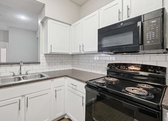 B1 kitchen with black appliances and white cabinets at Jefferson Place Apartments in Irving, TX