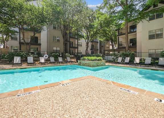 Sparkling pool surrounded by apartment buildings and pool loungers at Jefferson Place apartments in Irving, TX