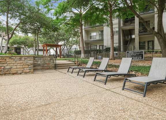 Pool loungers in the pool area with apartment buildings in the background at Jefferson Place apartments in Irving, TX