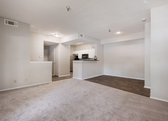 an empty living room with a kitchen in the background