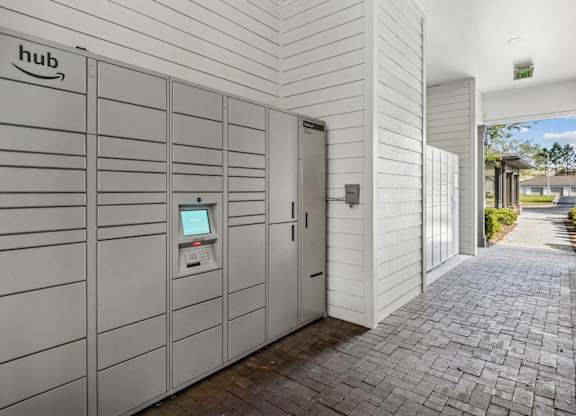 A row of Amazon hub vending machines are lined up on a brick walkway.