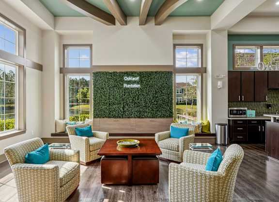 A clubhouse with a decorative grass wall and an Oakleaf Plantation sign surrounded by comfortable chairs and a table at Oakleaf Plantation Apartments in Jacksonville, FL