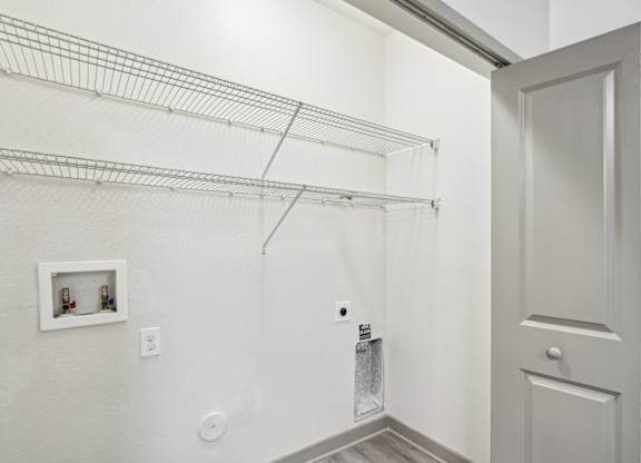 A laundry closet with washer and dryer connections and shelving at Oakleaf Plantation apartments in Jacksonville, FL.