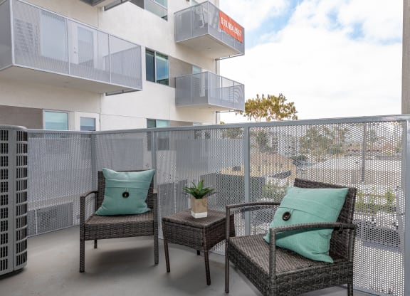 two wicker chairs sitting on a balcony with green pillows
