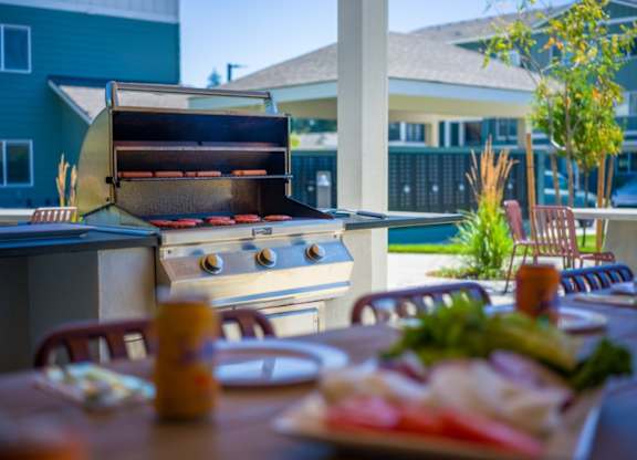 A barbecue grill is set up on a table with food and condiments on it.