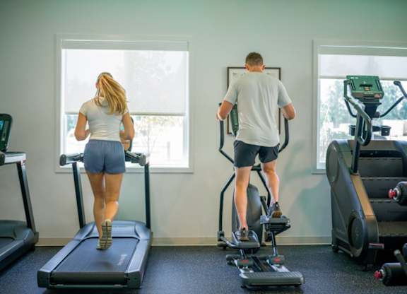 A man and a woman are exercising on treadmills in a gym.