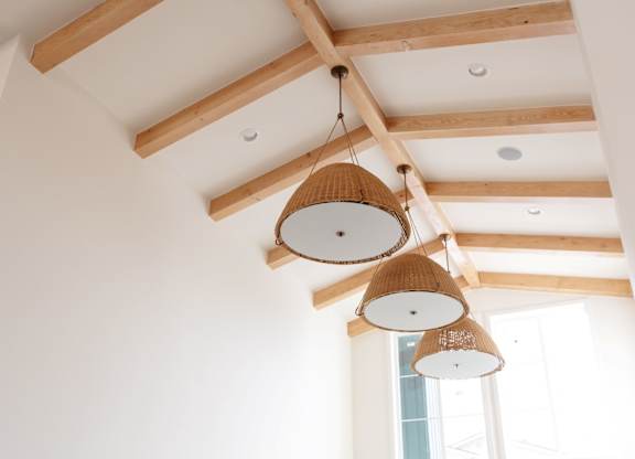Three hanging lamps with white shades are suspended from a wooden beam.