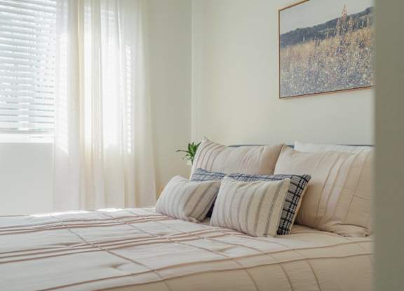 A bed with a white comforter and striped pillows with a plant on it.