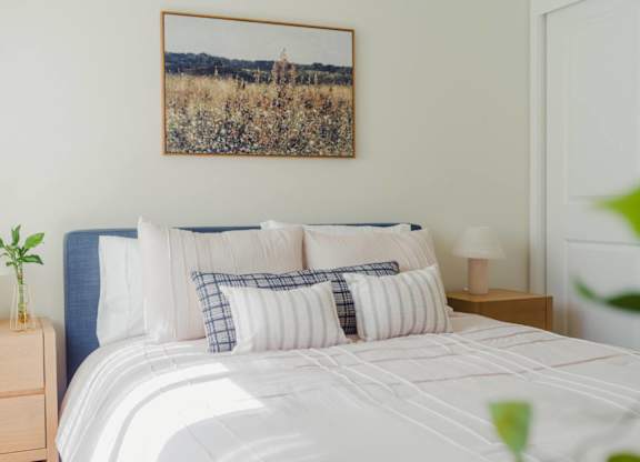 A bed with a white comforter and a landscape picture on the wall.