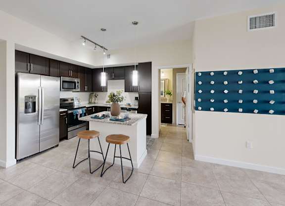 A kitchen with a refrigerator, stove, and bar stools.