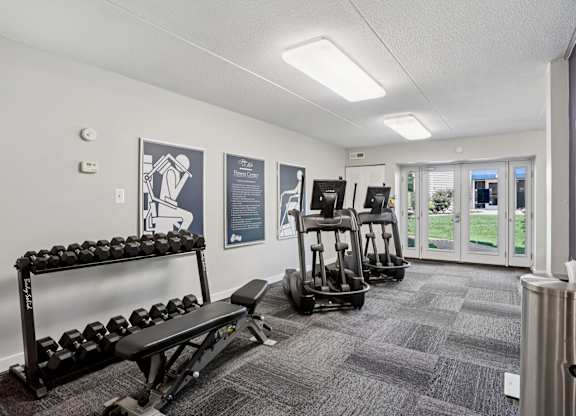 A gym with a variety of equipment including dumbbells, a bench, and a rowing machine.