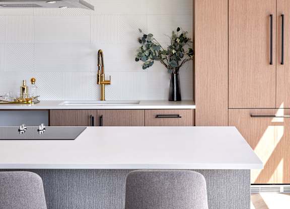A modern kitchen with a white countertop and grey bar stools.