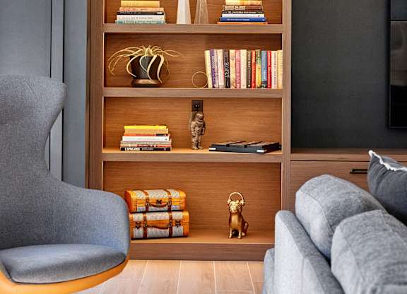 A grey chair sits in front of a bookshelf with various books and decorations.