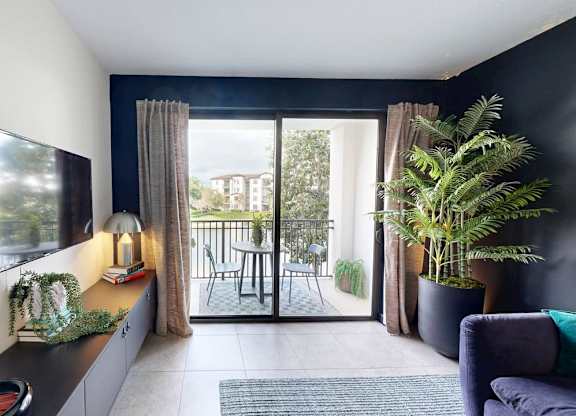 A living room with a flat screen TV on the wall and a sliding glass door leading to a balcony.