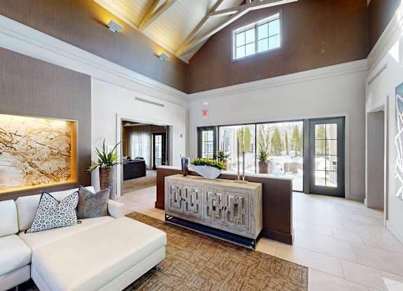 A white sofa with grey pillows is in the middle of a room with a wooden floor and a brown wall.