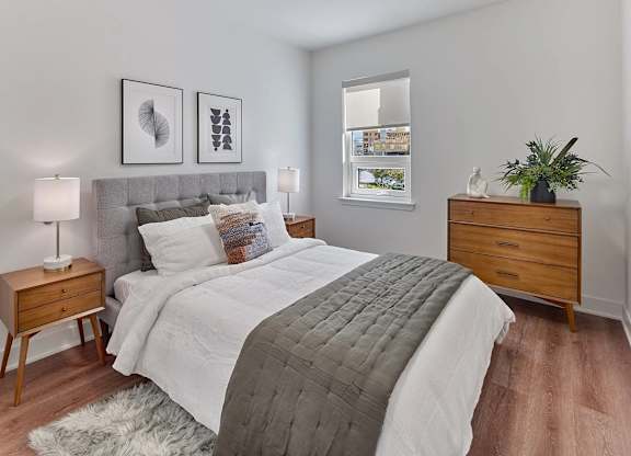 A bedroom with a bed, nightstand, and a plant.
