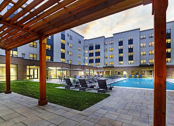 A pool surrounded by a patio with chairs and a pergola.