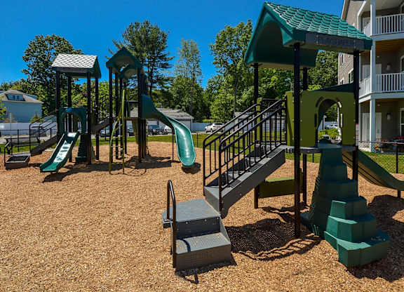 A playground with a green slide and a green and grey play structure.