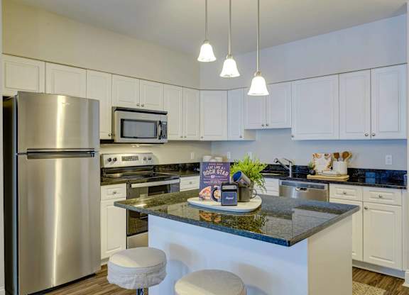 A kitchen with a refrigerator, microwave, and bar stools.