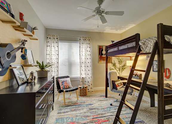 A room with a bunk bed and a chair with a colorful rug.