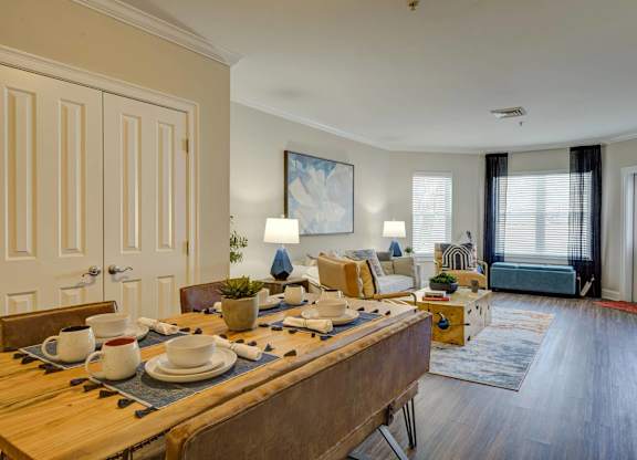 A dining table set with plates and cups is in the middle of a room with a couch and a bed in the background.