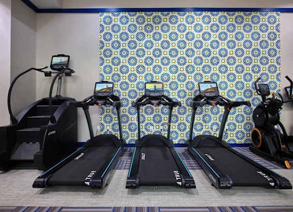 A row of treadmills are lined up in a row in front of a blue and white patterned wall.