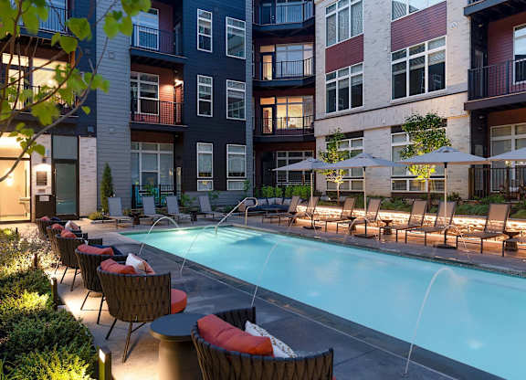 A pool surrounded by chairs and umbrellas in front of a building.