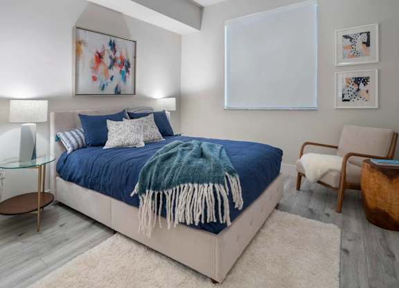 A bedroom with a bed, chair, and artwork on the wall.