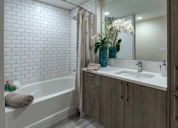 A white tiled bathroom with a white tub and a white sink.