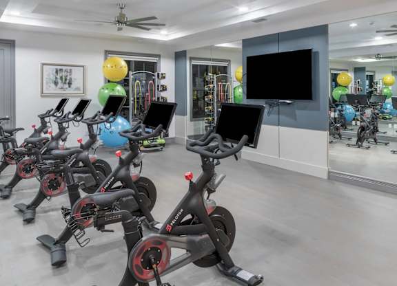 A room with a row of stationary bikes and a television.