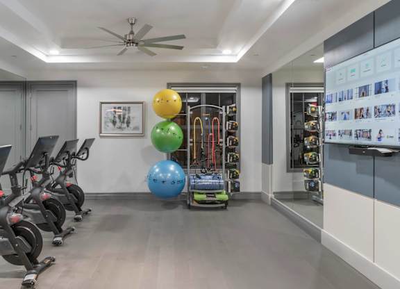 A gym with exercise equipment and a wall-mounted TV displaying fitness-related images.