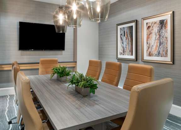 A conference room with a long table, chairs, and a television mounted on the wall.