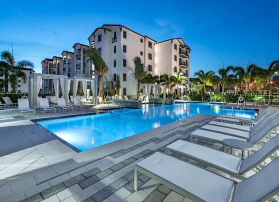 A large swimming pool surrounded by sun loungers and palm trees.