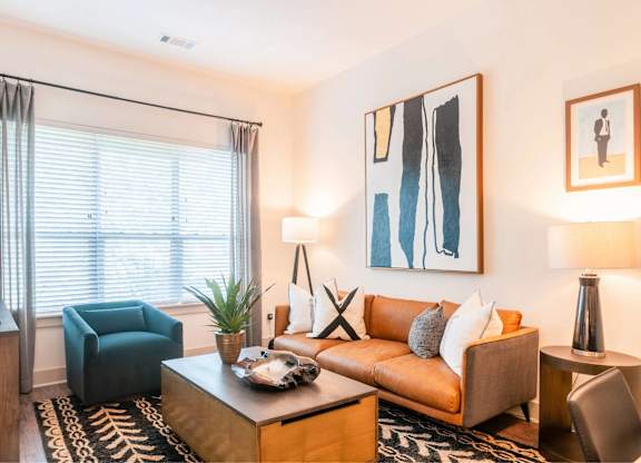 A living room with a brown couch, a blue chair, and a painting on the wall.