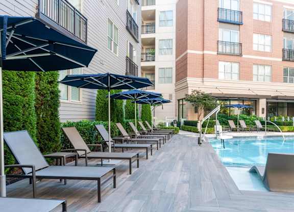 A pool area with lounge chairs and umbrellas in front of a building.