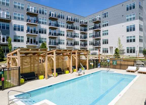 A large swimming pool is surrounded by sun loungers and a wooden pergola.