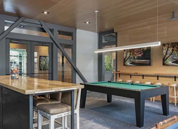 A pool table is in the middle of a room with a bar and a television.