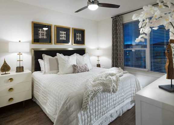 A bedroom with a large bed, a ceiling fan, and a dresser with a lamp on it.
