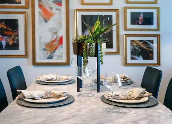 A dining table set with plates and glasses in front of a wall with framed pictures.
