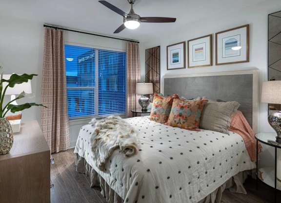 A bedroom with a bed covered in a white comforter with black dots, a ceiling fan, and a nightstand with a lamp.