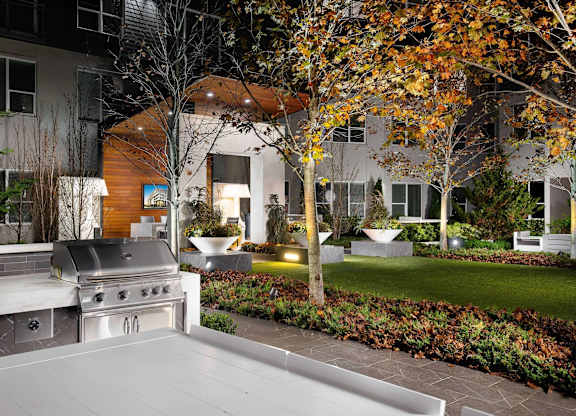 A BBQ grill is in the foreground of a backyard with a building in the background.