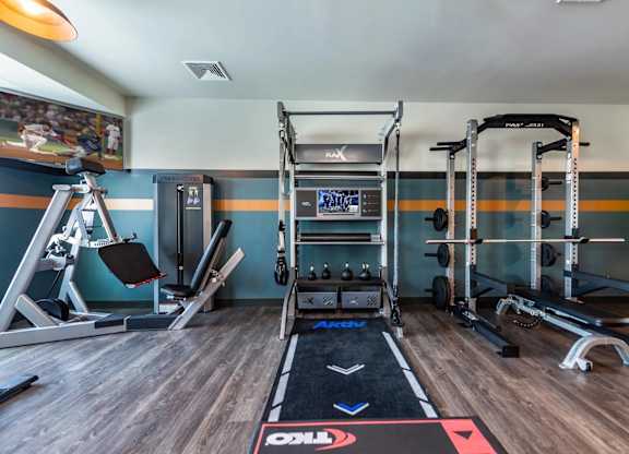 A gym with a wooden floor and a variety of equipment including a squat rack, bench press, and a weight machine.