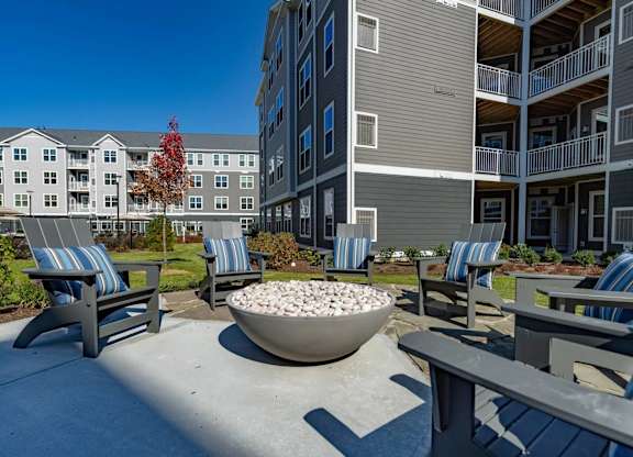 A concrete patio with a bowl of rocks in the middle and chairs around it.
