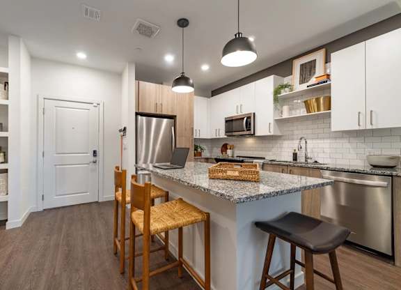 A kitchen with a white counter top and wooden chairs.