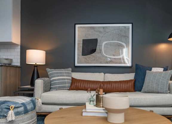 A modern living room with a grey couch, a coffee table, and a large abstract painting on the wall.