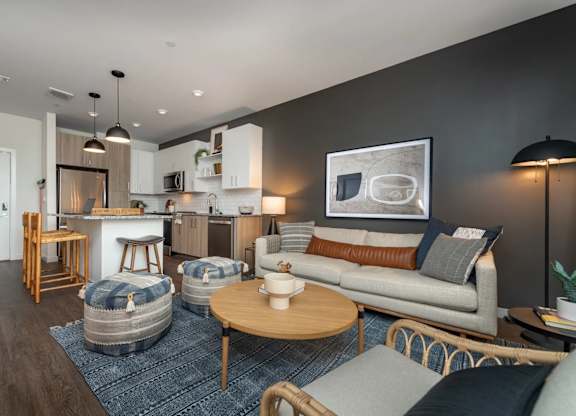 A modern living room with a grey couch, a wooden coffee table, and a kitchen area in the background.