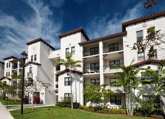 A white apartment building with balconies and trees in front.