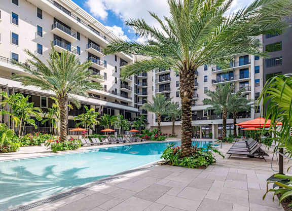 A pool surrounded by palm trees and lounge chairs.