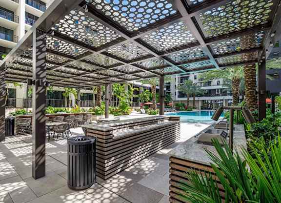 A pool area with a sun shade and a trash can.