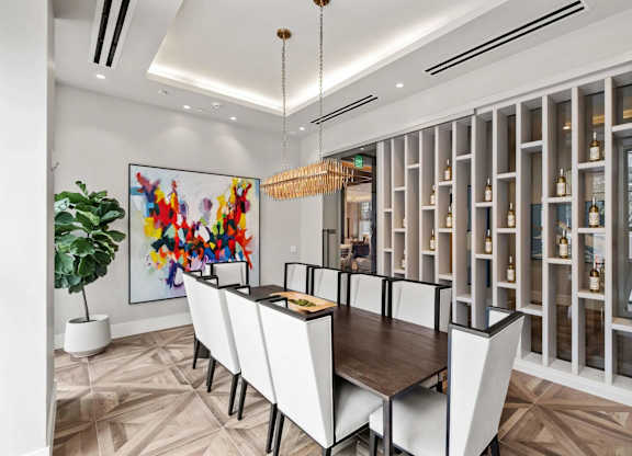 A dining room with a large painting on the wall and a wine rack in the background.